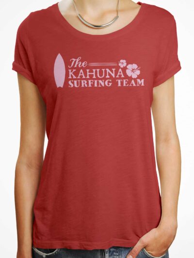 Red t-shirt displaying 'The Kahuna Surfing Team' logo with a pink surfboard outline and hibiscus flowers on the chest area, worn by a person.