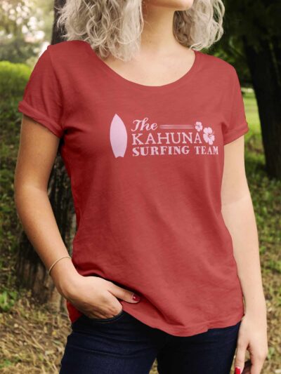 Person wearing a red T-shirt with The Kahuna Surfing Team logo outdoors, partial upper body visible and palms facing inward.