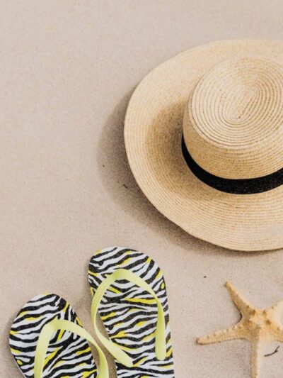 Beach scene with a straw hat, zebra-pattern flip-flops with yellow straps, and a starfish on sand.