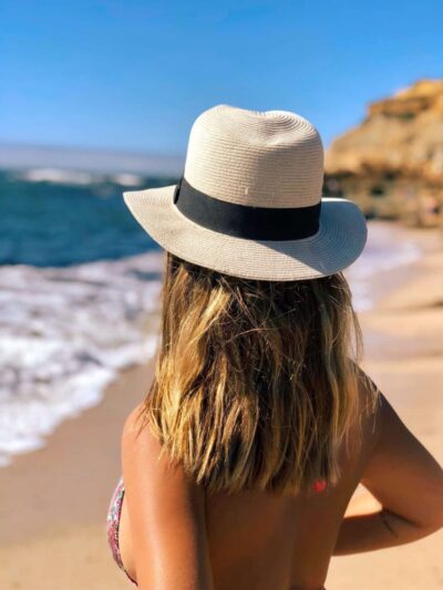 Back view of a woman at the beach wearing a wide-brimmed straw hat with a black band, ocean waves in the background](noting: adjust for image alt)