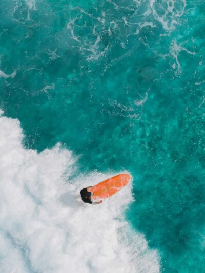 Surfer riding a bright orange surfboard on turquoise ocean with white waves nearby.