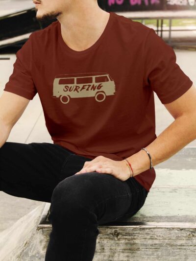 Person sitting on concrete steps wearing a maroon t-shirt with a beige van graphic and the word 'SURFING' on the chest.