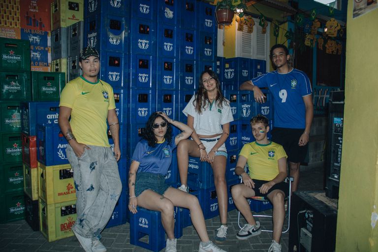 Group of young adults in Brazil football jerseys posing with AmBev crates outdoors.