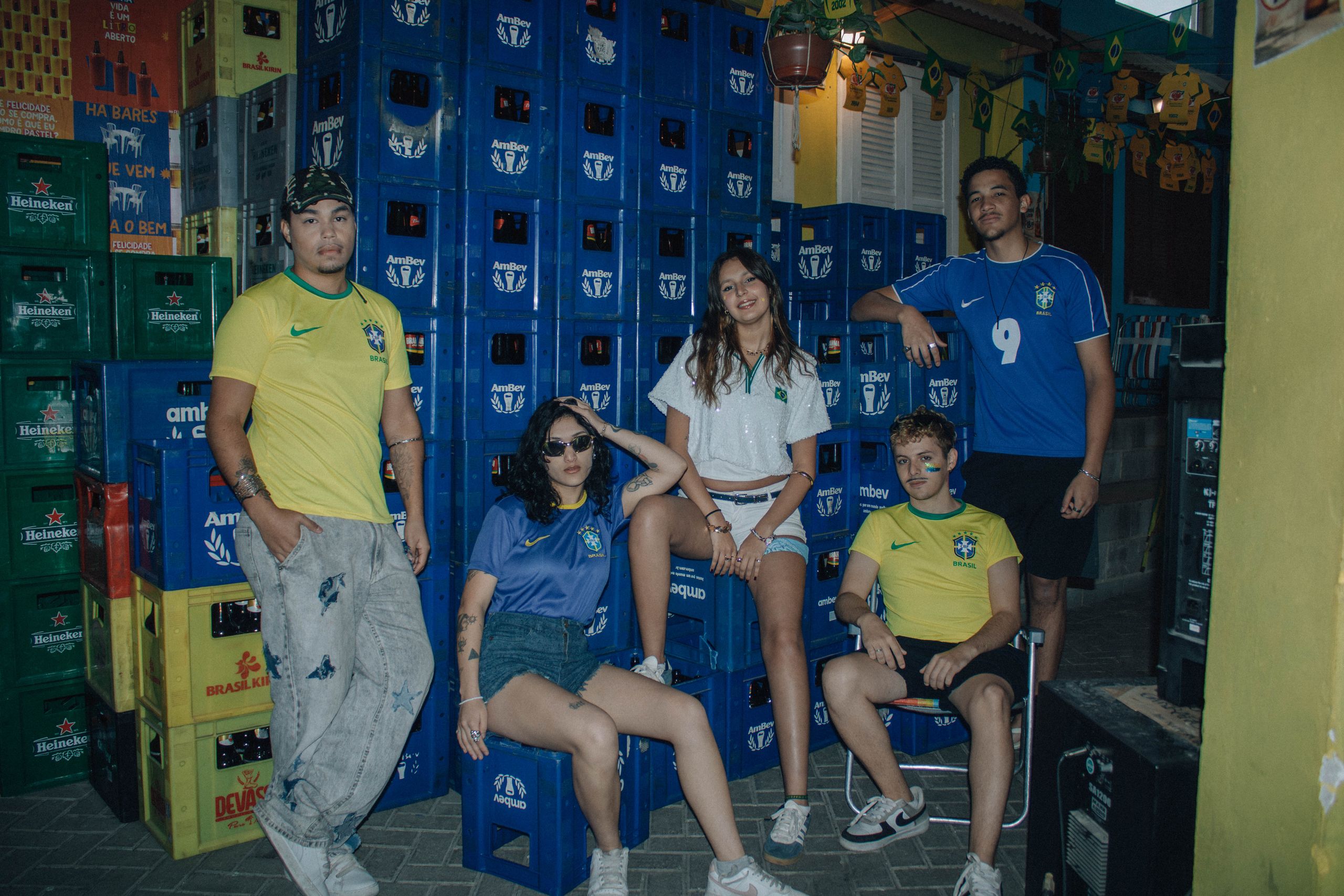 Group of young adults in Brazil football jerseys posing with AmBev crates outdoors.