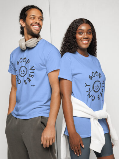 Two people in light blue t-shirts stand back-to-back, smiling at the camera; the man wears headphones around his neck against a neutral backdrop.