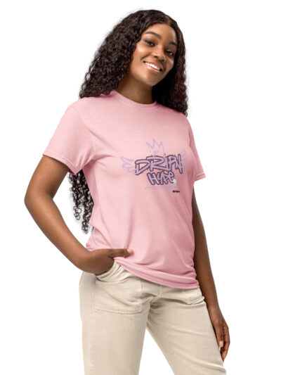 Smiling woman wearing a pink graphic T‑shirt and beige pants, angled to the side.