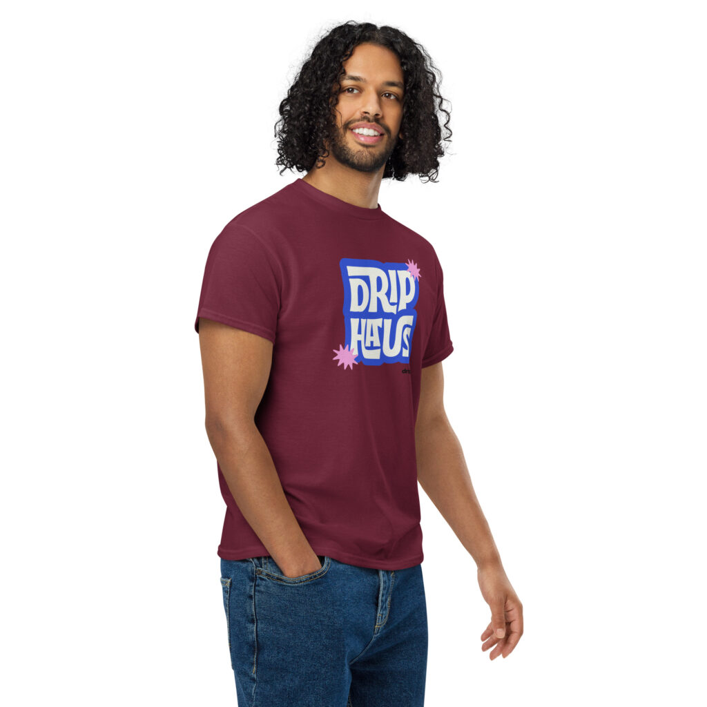 Portrait of a man with long curly hair wearing a maroon graphic t-shirt, facing slightly right and smiling.